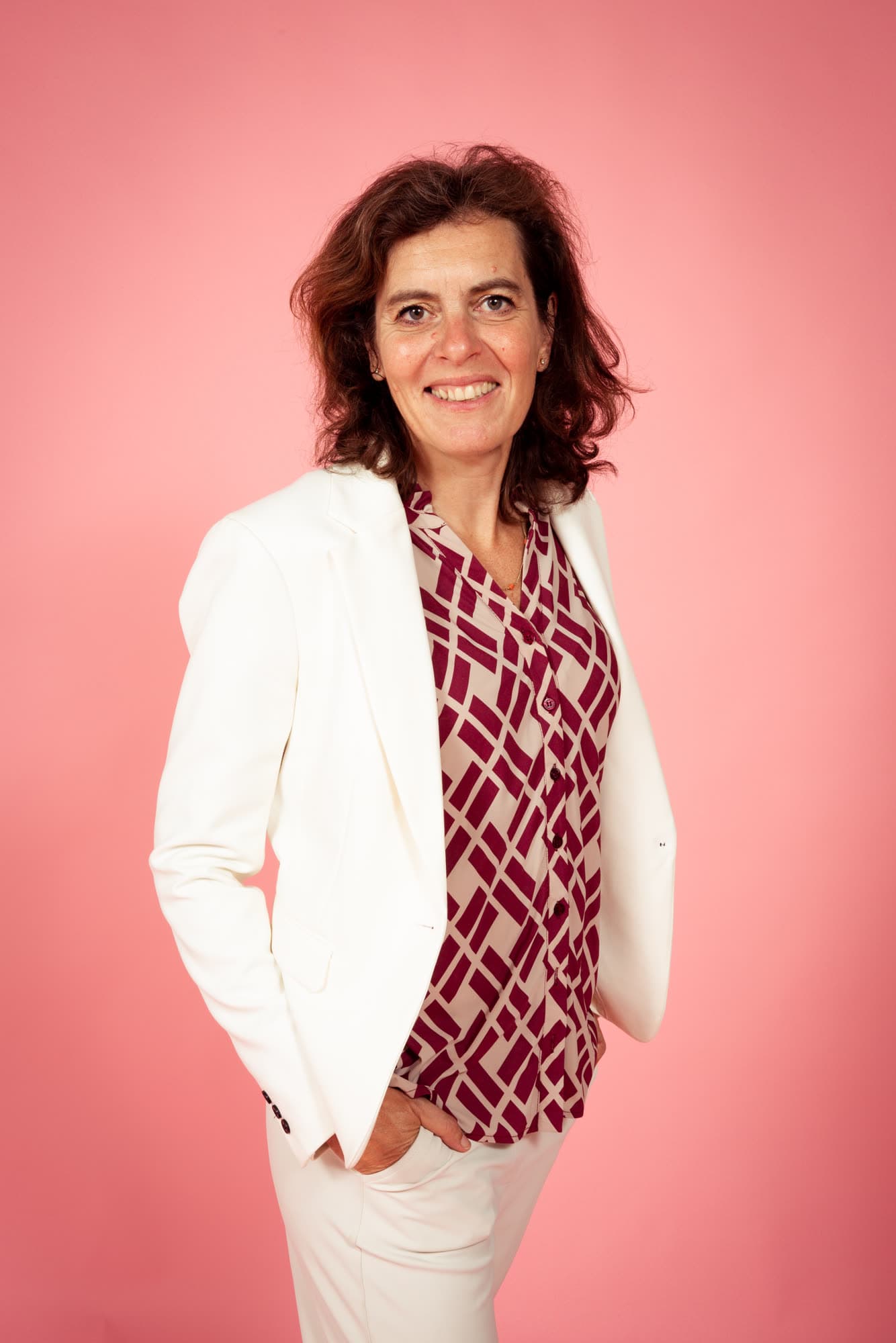 Emily Staphorst staat lachend met haar handen in haar zakken tegen een roze achtergrond